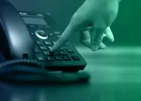 Uma mão apertando um botão em um telefone fixo.